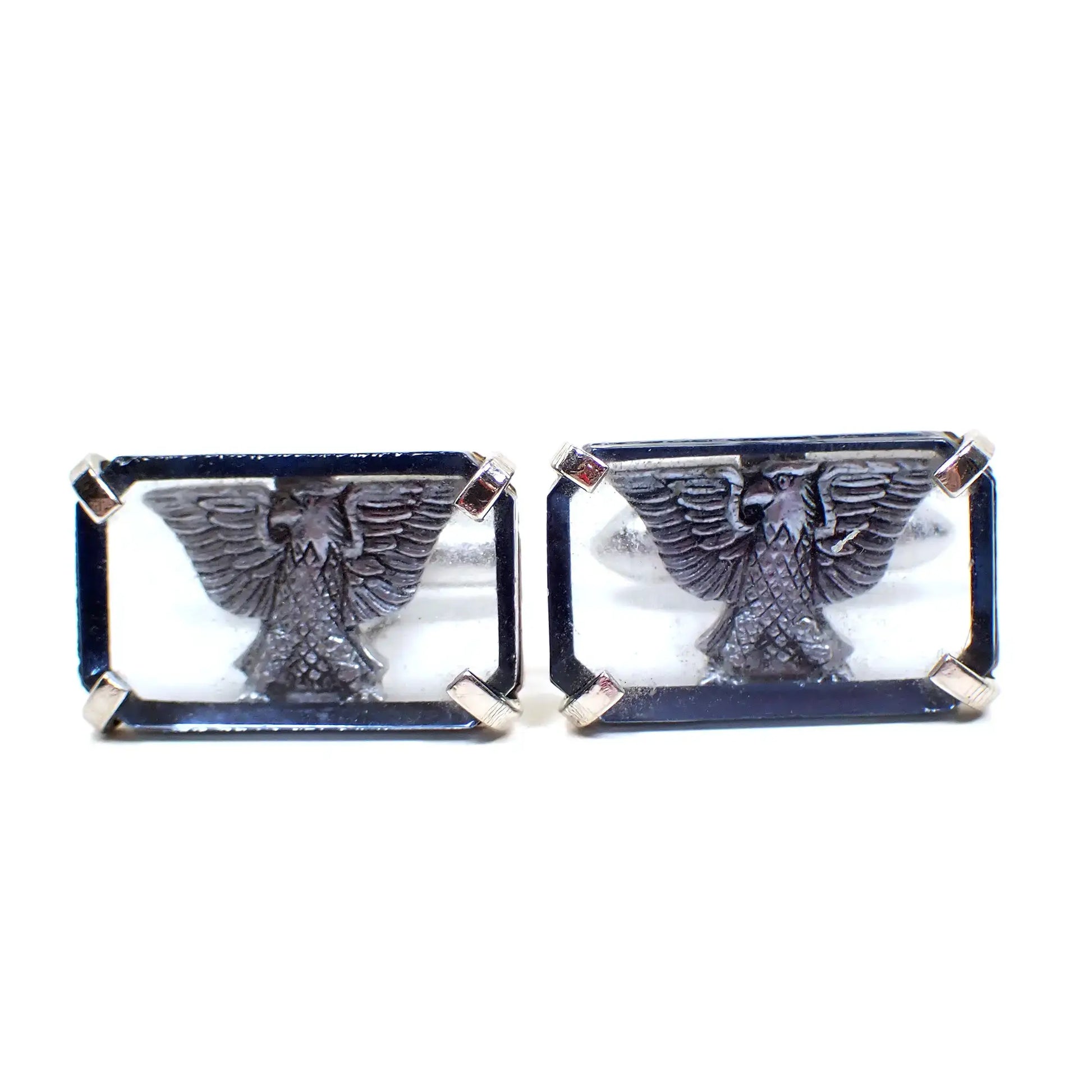 Front view of the retro vintage Swank cufflinks. The metal is silver tone in color. They are shaped like rectangles and have a transparent blue glass front with a silver tone eagle design behind it. The eagle has his wings spread.