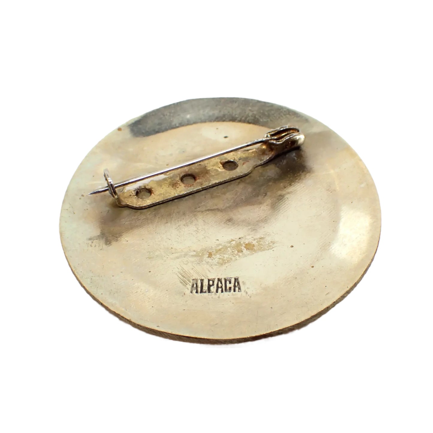 Photo of the back side of the brooch. The pin has a C style tuck under clasp. The metal is darkened, especially near the pin area. Alpaca can be seen stamped on to the metal at the bottom of the brooch.