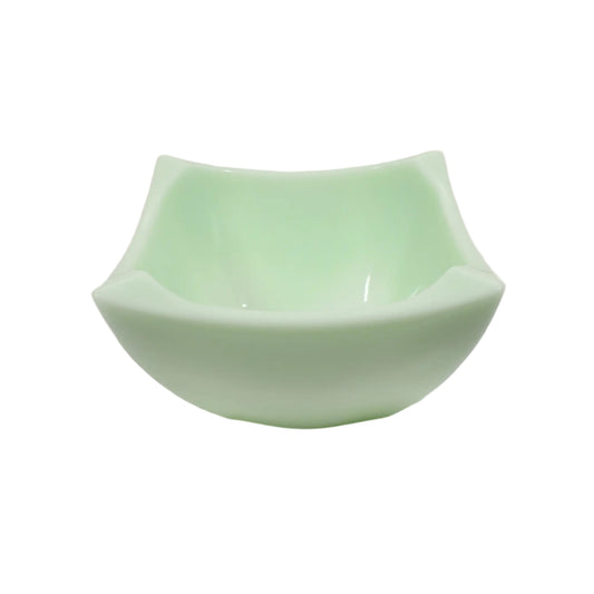 Angled view of the handmade square resin bowl. It's has flared out angled ends and is a light lime cream pastel green in color with hints of white.