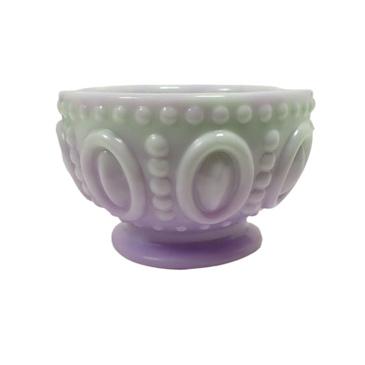 Side view of the handmade resin footed bowl. it is round with a dot and oval pattern around the outside. It has mixed colors of light pastel purple and lime cream green.