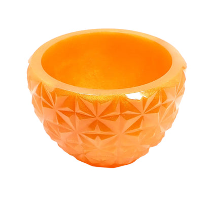 Angled side view of the pearly orange faceted bowl. It is round with a tapered bottom and faceted design around the outside. The resin is a pearly orange in color.