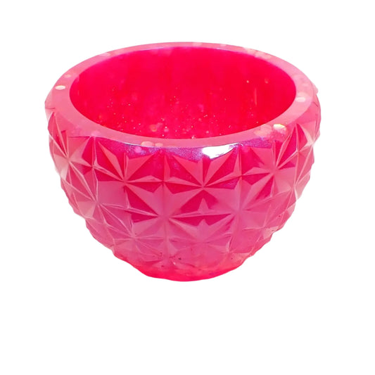 Angled side view of the handmade resin faceted bowl. It's round with a tapered bottom and retro style faceted design. There is some flashes of color seen from the glitter at the top and inside area of the bowl.