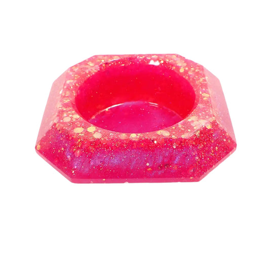 Angled view of the handmade resin octagon decorative bowl. It has pearly bright pink resin with iridescent chunky glitter mostly around the top edge.