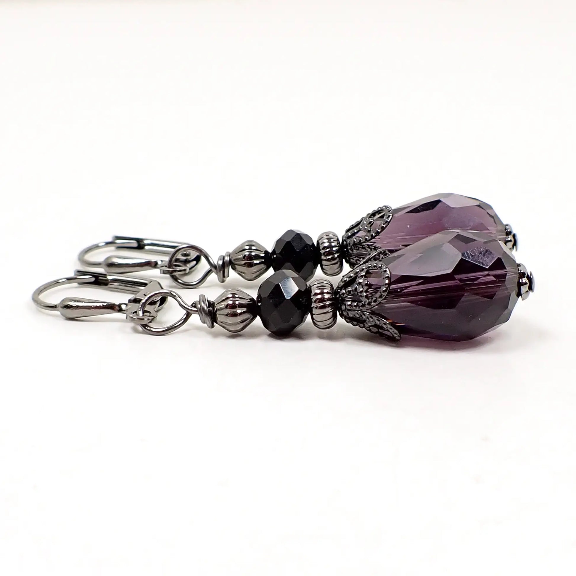 Side view of the handmade purple and black teardrop earrings. There are spacer beads and a filigree bead cap for a vintage style appearance and Goth look to the earrings.