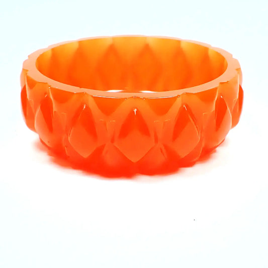 Angled side view of the handmade neon reddish orange resin ring dish. It is round with a carved like diamond shaped design all the way around the outside. The resin is shiny and semi translucent in a neon reddish orange color. 