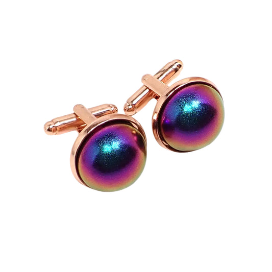 Angled view of the cufflinks. The settings are rose gold in color. There are domed round resin cabs on the front with matte metallic shades of pink, blue, purple, and a few other colors as they move around in the light.