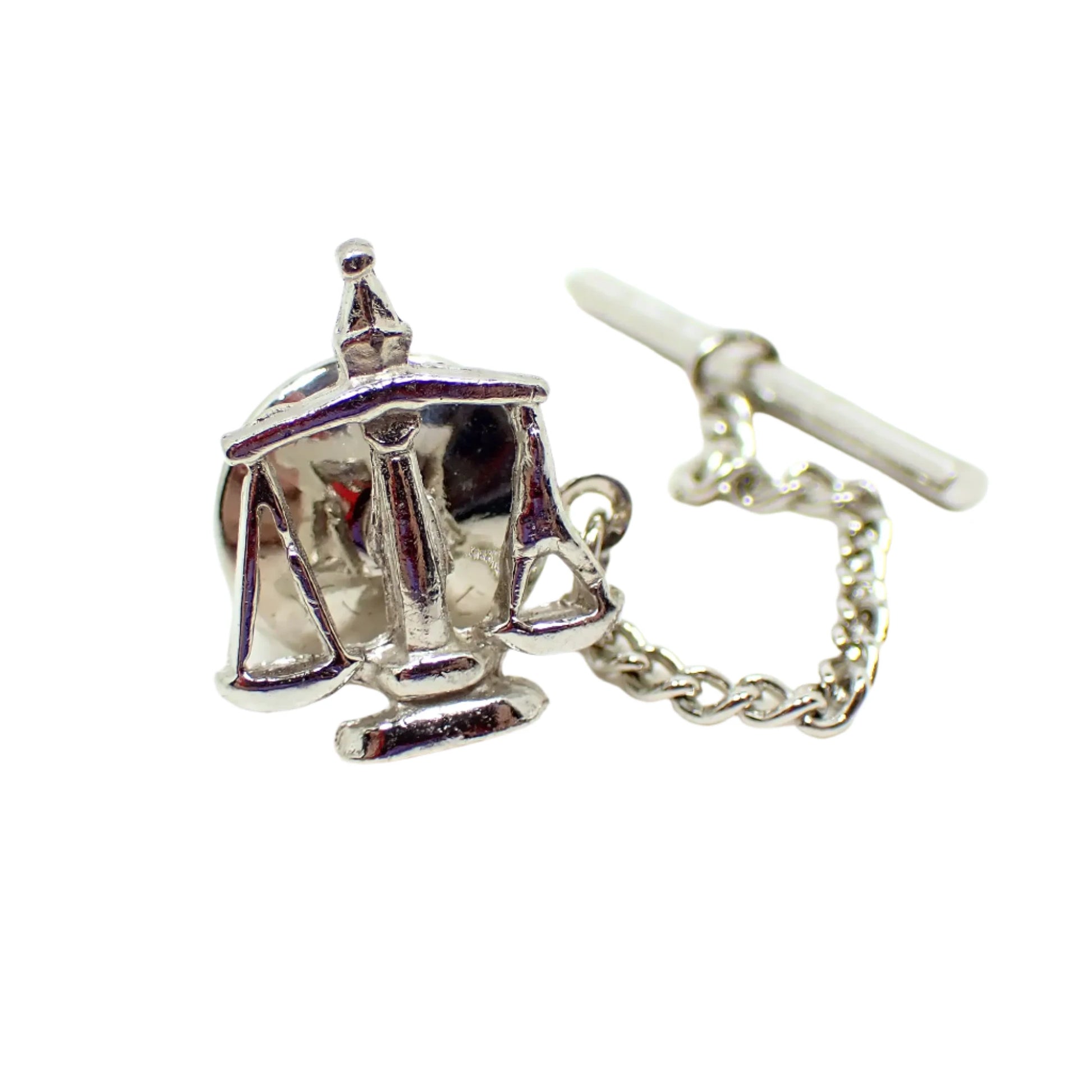 Another full view of the vintage Scales of Justice tie tack. The silver tone metal is shiny and reflections of items in the room can be seen.