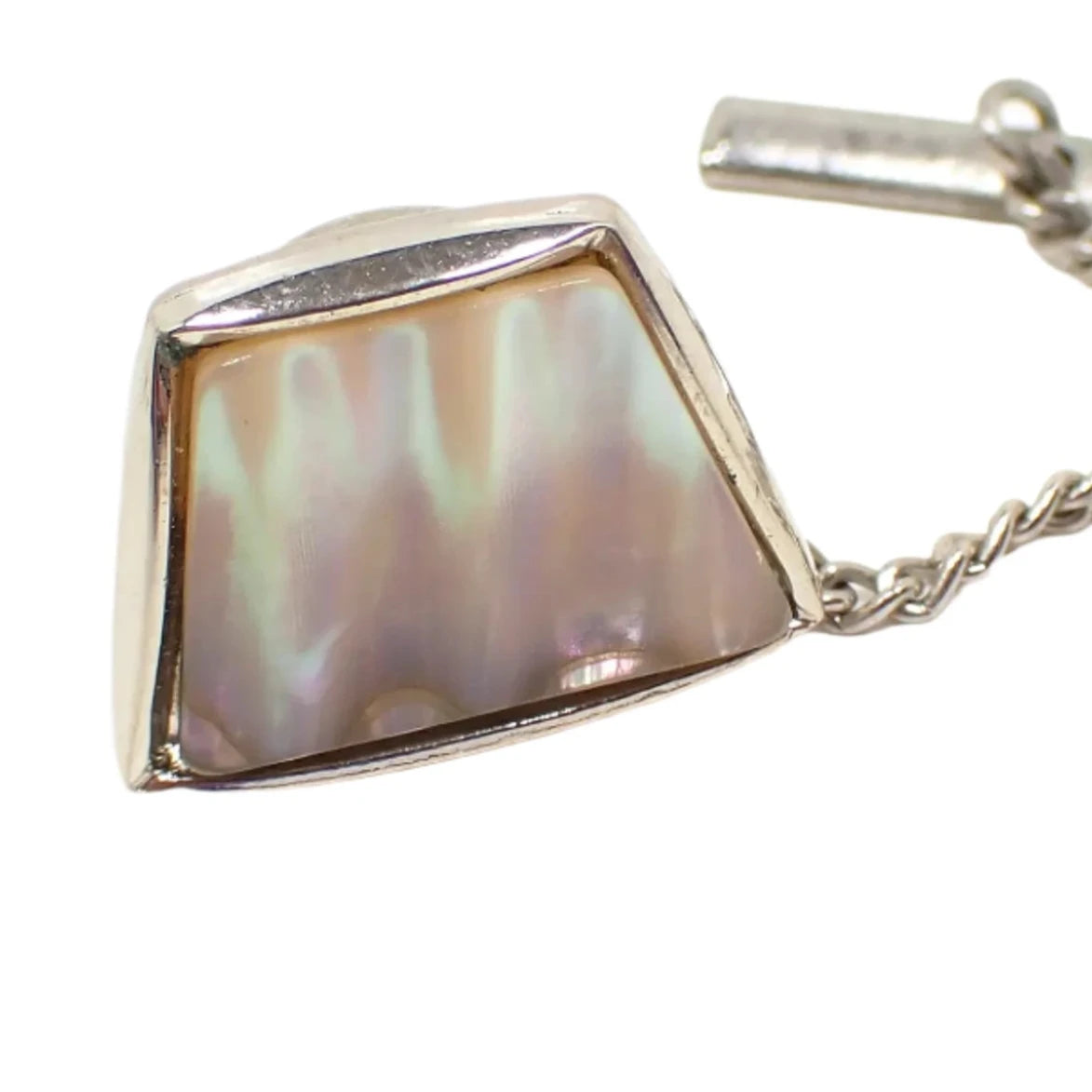 Enlarged front view of the vintage trapezoid shaped mother of pearl shell tie tack. The shell has a light pink color with flashes of other colors as the light hits it. The metal is silver tone in color.