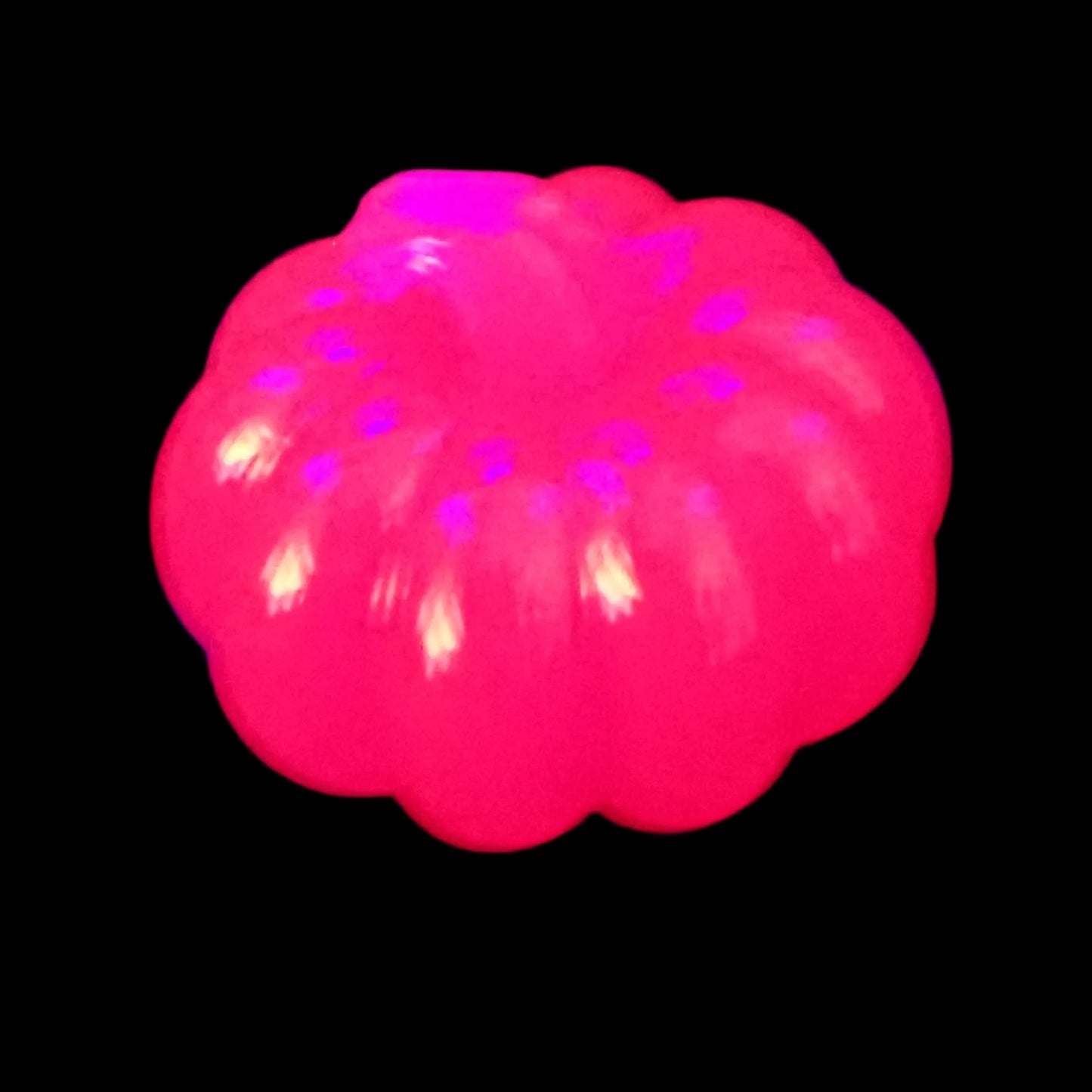 Photo of the shiny neon pink pumpkin fluorescing bright pink under a UV light.