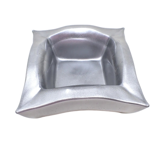 Angled top view of the handmade resin Retro Atomic style square decorative bowl. It is large with curvy sides and pinched corners. The top sides are curved upward and the sides are curved inwards. The resin is shiny and opaque in a metallic silver color.
