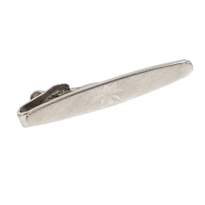 Angled front view of the Swank vintage tie clip. The front has a textured brushed matte pattern with an engraved starburst design in the middle.
