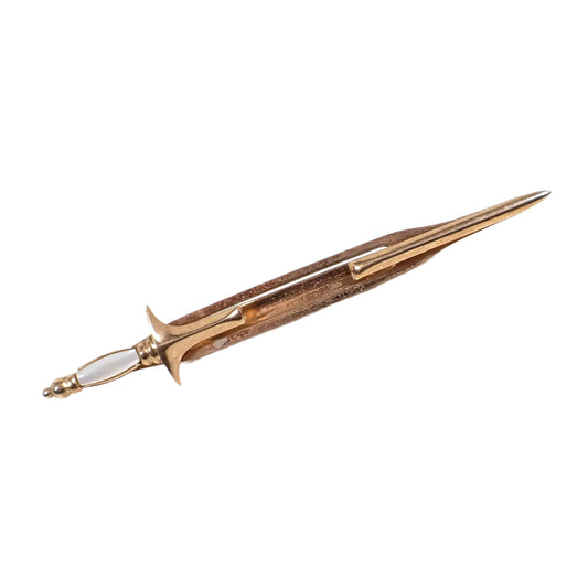 Angled view of the Swank Mid Century vintage tie bar. It is shaped like a rapier sword with a clip on each side to hold it onto the tie as well as a slide on the back. The metal is gold tone in color and the handle has a pearly white mother of pearl shell cab. 