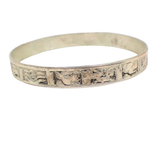 Angled side view of the bangle bracelet. There are rectangles around the outside of the bangle and each one has either a raised symbol or animal symbol in them.