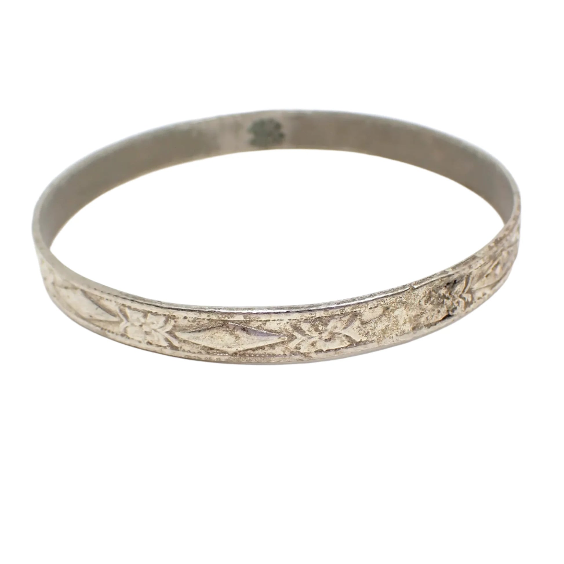 Angled view of the Mid Century vintage Taxco bangle bracelet. It is antiqued silver in color with a raised floral and diamond shape design all the way around the outside of it.