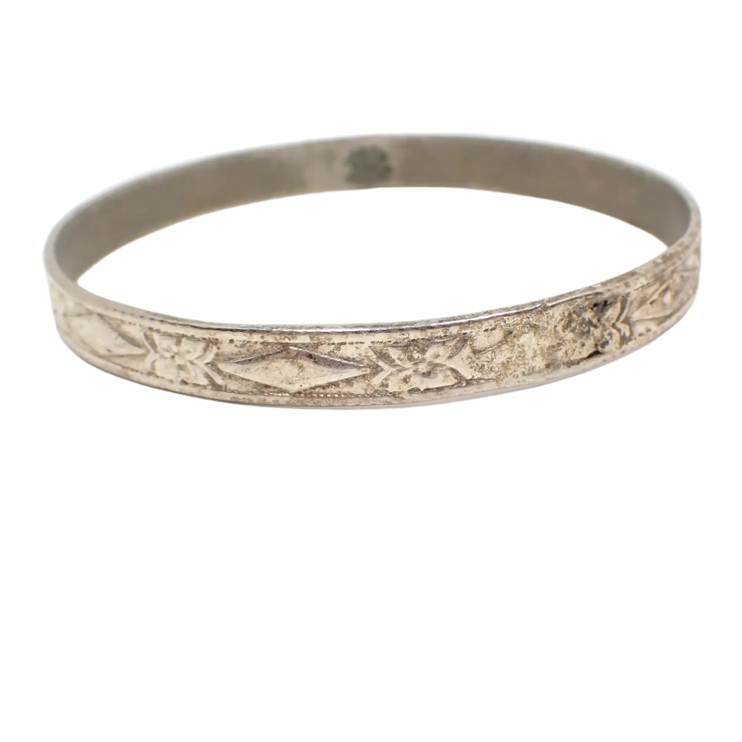 Another angled view of the bangle bracelet. Here more of the raised flower and diamond shaped design can be seen as well as the inside of the bangle which has a darkened patina.