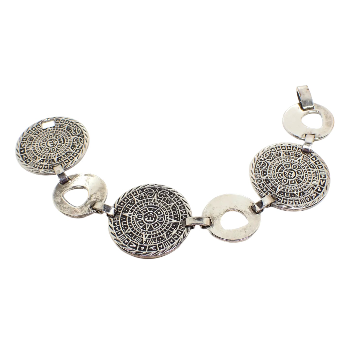 Top view of the vintage Taxco Mayan calendar bracelet. The metal is antiqued silver in color. There are three large round calendar links with a raised design and blackened recessed areas. There are also three round links in between that have a rounded triangle cut out design on them. There is a snap lock clasp on the end.