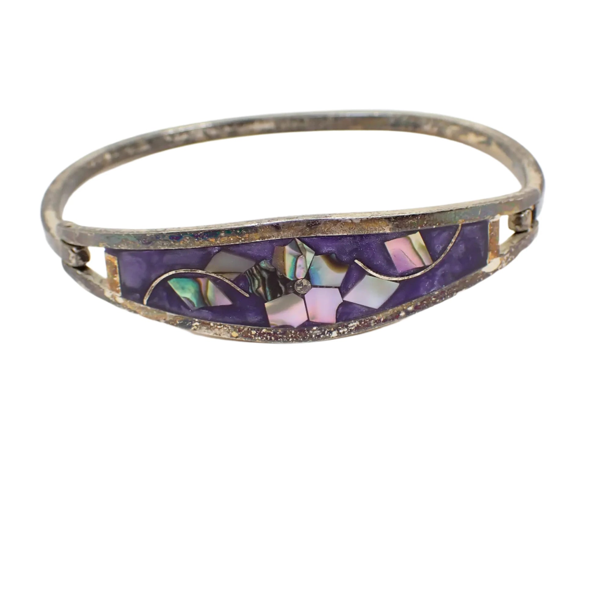 Front view of the vintage Taxco hinged bangle bracelet. The metal has a very darkened patina to a dark gray with some blackened areas. The front has pearly purple enamel with inlaid pieces of abalone shell forming a flower and two sets of leaves.