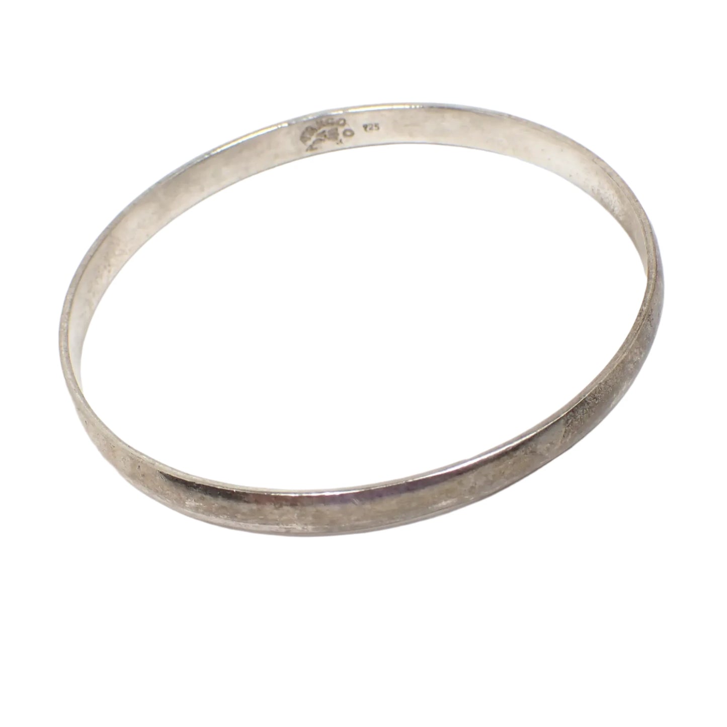 Angled view of the bangle bracelet. It has a smooth rounded exterior and has a darkened patina from age to an antiqued silver color. The Taxco marking and 925 can be seen on the inside of the bangle in this phot.