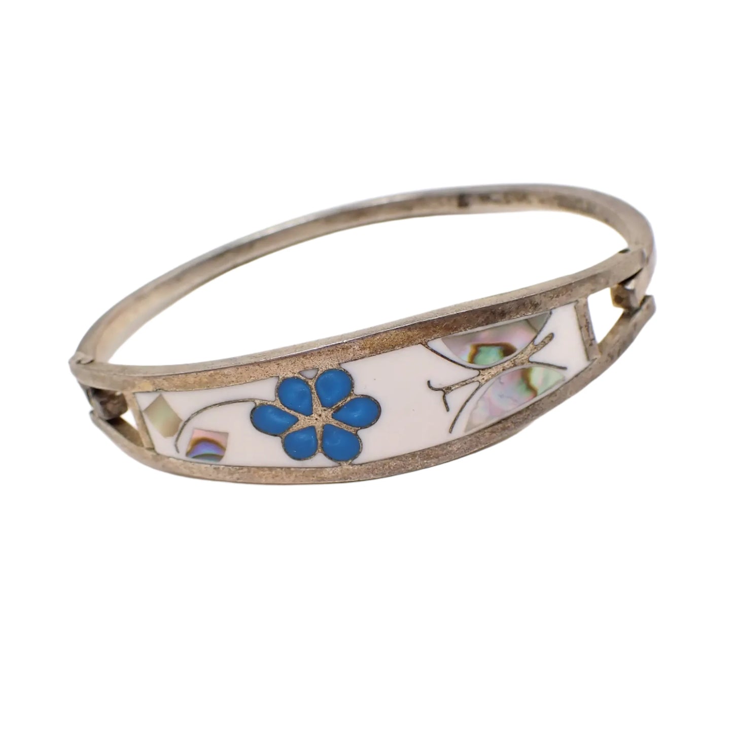 Angled view of the vintage Taxco hinged bangle bracelet. Here the butterfly and flower leaves with inlaid abalone shell pieces can be seen clearly. There are flashes of different colors in the shell.