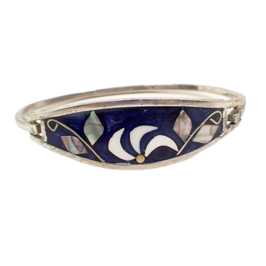 Front view of the floral vintage hinged bangle bracelet. The metal is silver tone in color. There is a hinge on one side and a clasp on the other. The front is curved and wider in the middle. There is a half flower design at the bottom with white enameled petals. On each side of the flower are curved metal stems with inlaid abalone shell leaves.