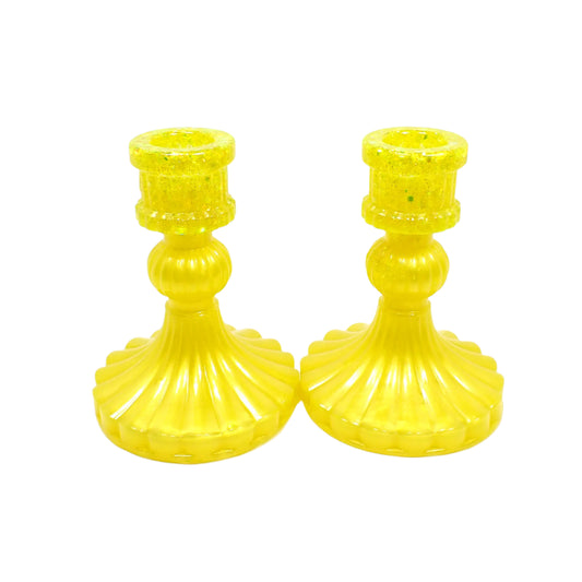 Angled side view of the handmade resin candle holders. The resin is bright pearly yellow in color and there is chunky iridescent glitter on the tops. The candlestick holders have a a vintage style design with barrel shaped tops, sphere shaped middles, and flared round bottoms. The sides are fluted. Great for Spring and Summer home decor use.
