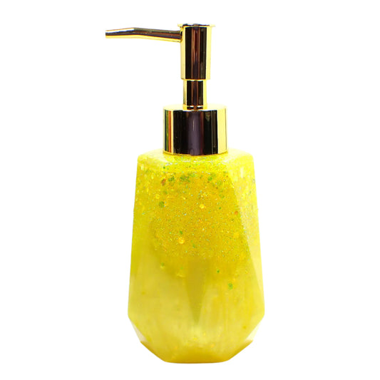 Side view of the handmade yellow glitter resin soap dispenser. It has a long hexagon faceted shape with tapered top and flared bottom. The resin is shiny and opaque in a pearly lemon yellow color. The top area has chunky iridescent yellow glitter for sparkle and glitz. 