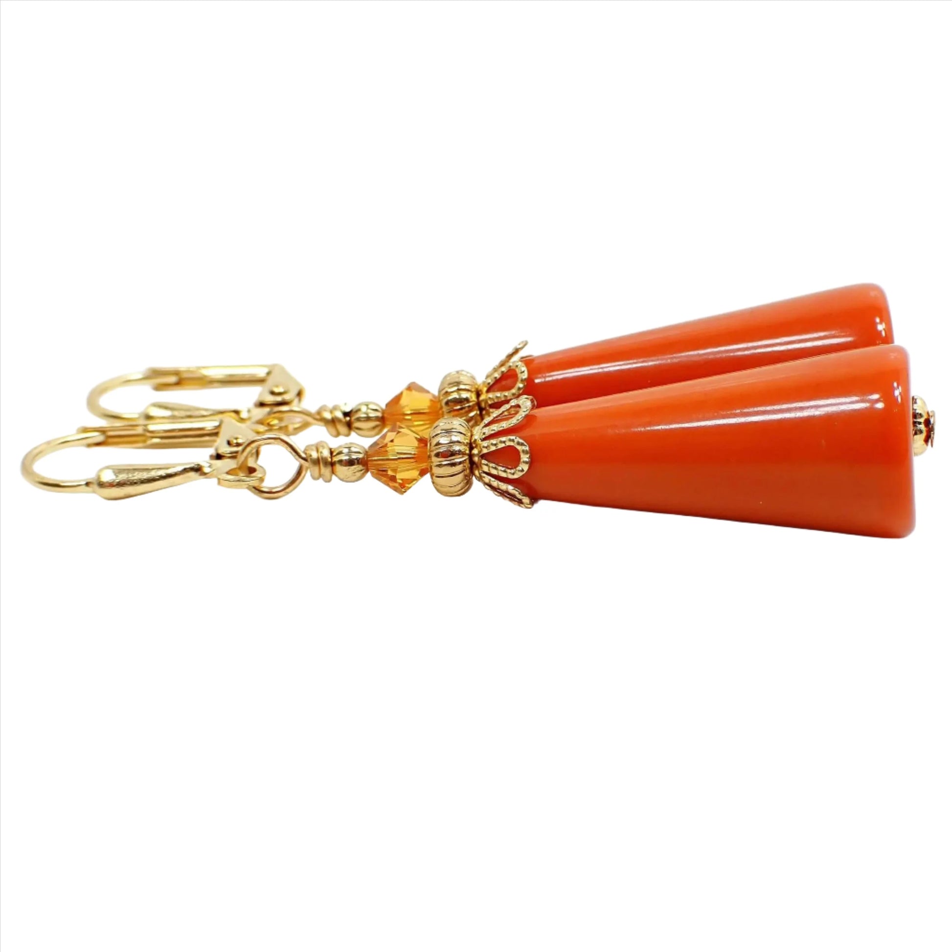 Side view of the handmade geometric cone earrings. The metal is gold plated in color. There are bright orange faceted glass crystal beads on the top. The bottom cone shaped bead is a vintage lucite bead in a dark burnt orange color.