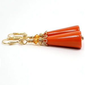 Side view of the handmade geometric cone earrings. The metal is gold plated in color. There are bright orange faceted glass crystal beads on the top. The bottom cone shaped bead is a vintage lucite bead in a dark burnt orange color.
