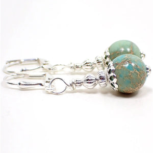 Side view of the handmade sea sediment jasper earrings. The metal is silver plated in color. There are smaller sized round sphere shaped beads at the bottom that are aqua blue in color with some shades of green and veins marbled in with brown, white, cream, and reddish tones.