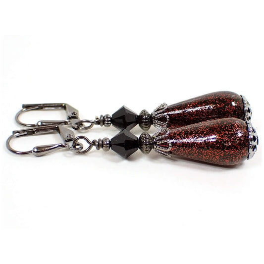 Side view of the handmade earrings with vintage glitter beads. The metal is gunmetal gray in color. There are black faceted glass beads at the top. The bottom vintage beads are black plastic with red glitter on the outside. They are teardrop in shape.