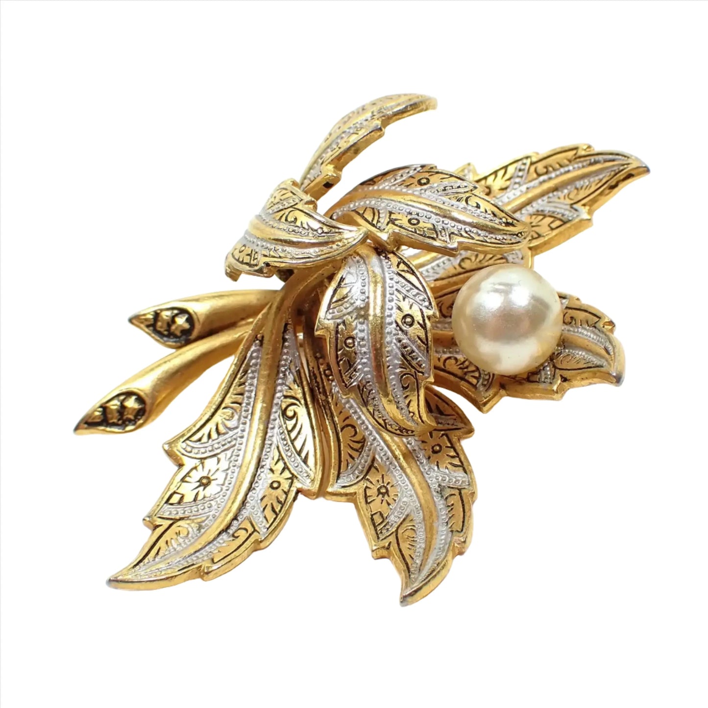 Enlarged view of the Mid Century vintage faux pearl Damascene brooch pin. The metal is mostly gold tone in color and has metallic silver and black painted design. There are numerous curled leaves and a plastic faux pearl on one of the leaves.