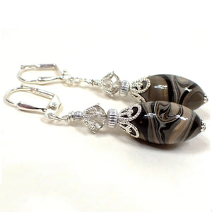 Side view of the handmade drop earrings with vintage lucite beads. The metal is silver plated in color. There are faceted glass crystal beads at the top in a very light gray color. The bottom oval beads are lucite and have a swirled marbled pattern with shades of gray, brown, black, and white. Each bottom bead is different in pattern from the other for a unique look.