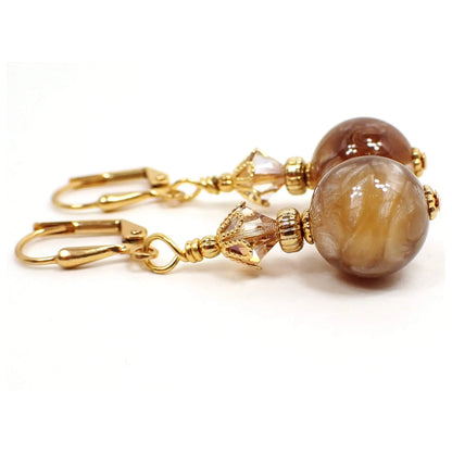 Side view of the handmade drop earrings vintage vintage lucite beads. The metal is gold plated in color. There are faceted glass crystal beads at the top if a light brown color with hints of orange. The bottom lucite beads are round and have pearly marbled swirls of brown and peach tones.