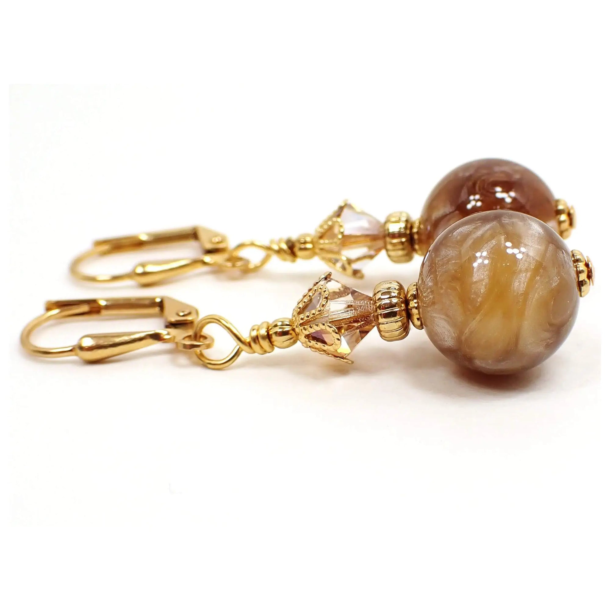 Side view of the handmade drop earrings vintage vintage lucite beads. The metal is gold plated in color. There are faceted glass crystal beads at the top if a light brown color with hints of orange. The bottom lucite beads are round and have pearly marbled swirls of brown and peach tones.