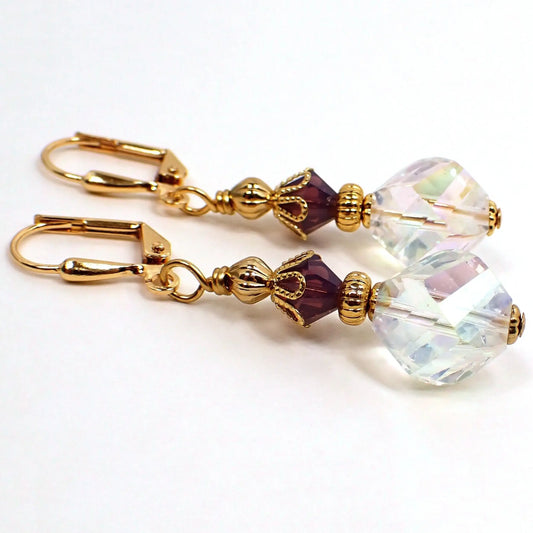 Side view of the handmade glass crystal beaded earrings. The metal is gold plated in color. There is a purple bicone bead at the top and a faceted angled teardrop like bead at the bottom with a light AB coating.