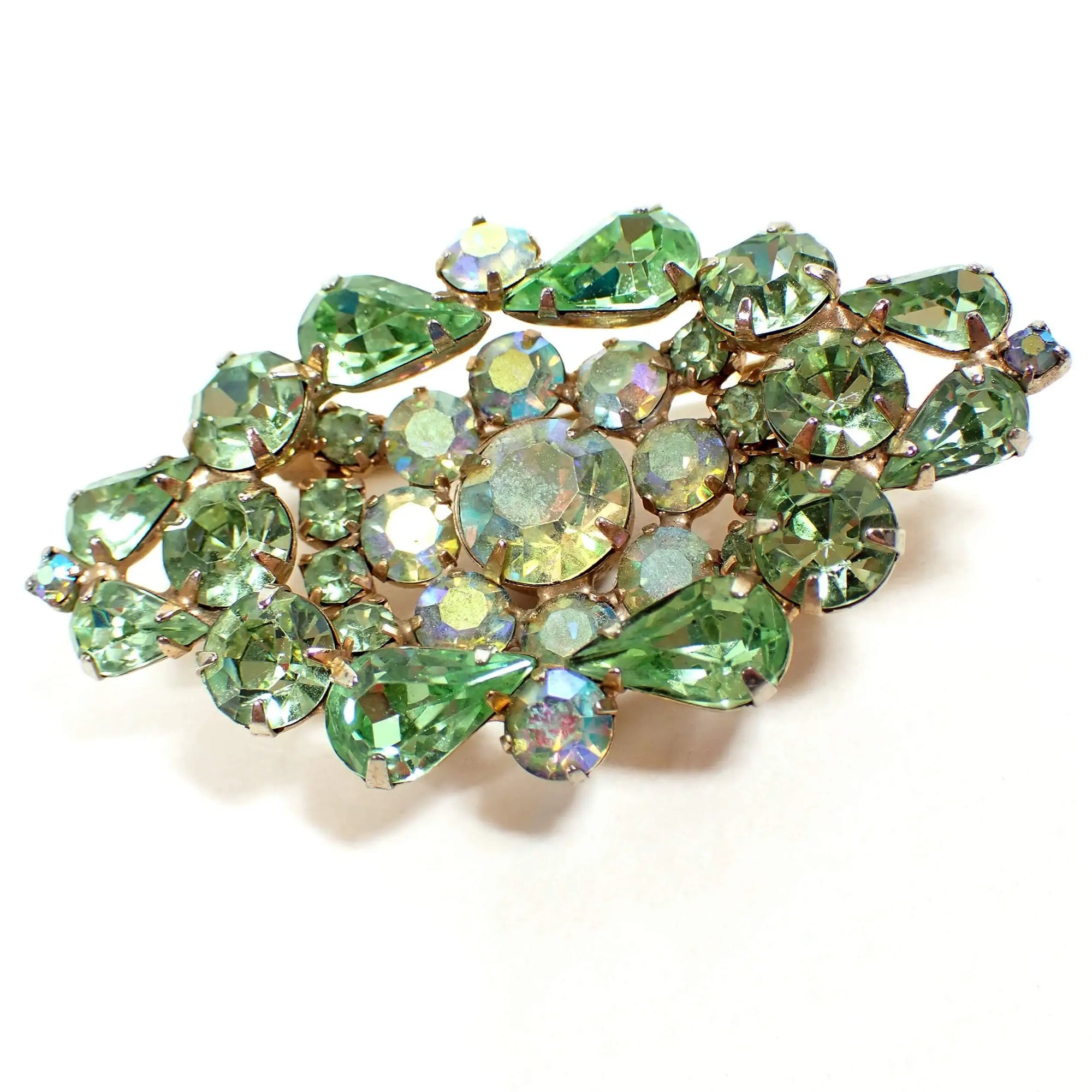 Front view of the Mid Century vintage Weiss crystal rhinestone brooch pin. The metal is gold tone in color and it is shaped like a tiered wide diamond shape. There are green teardrop and round rhinestones and AB round green rhinestones making up the entire front of the brooch.