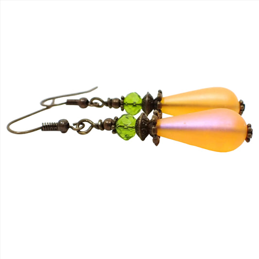 Side view of the handmade teardrop earrings made with vintage lucite beads. The metal is antiqued brass in color. There is a faceted green crystal glass rondelle bead at the top and a frosted orange lucite teardrop bead at the bottom.
