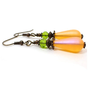 Side view of the handmade teardrop earrings made with vintage lucite beads. The metal is antiqued brass in color. There is a faceted green crystal glass rondelle bead at the top and a frosted orange lucite teardrop bead at the bottom.