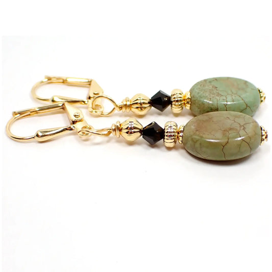 Side view of the handmade magnesite earrings. The metal is gold plated in color. There are black faceted glass beads at the top. The bottom gemstone beads are dyed olive green in color and have some hints of brown and a brown vein like design.