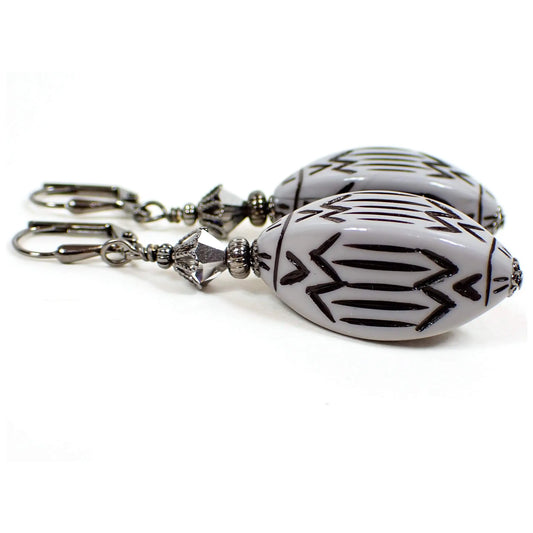 Side view of the large handmade drop earrings with vintage lucite beads. The metal is gunmetal gray in color. There is a metallic silver faceted glass bead at the top. The bottom lucite bead is a faceted pointed oval shape and is gray in color with an etched black Southwestern style design.