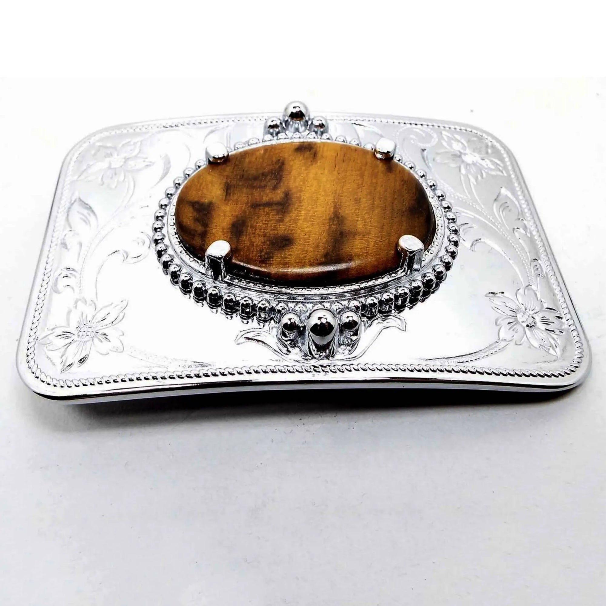 Front view of the retro vintage Reddscraft myrtlewood vintage belt buckle. The buckle is silver tone in color with a stamped floral design around the corners. The middle has a prong set oval cab of myrtlewood wood in shades of brown.