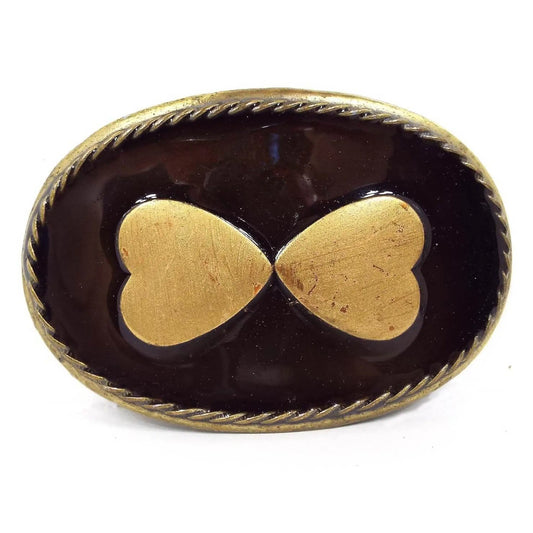 Front view of the Midwestern Mfg belt buckle. It is oval and antiqued brass in color. The front has two hears with the bottom of the hearts pointing inwards. The background on the front is enameled in dark brown.