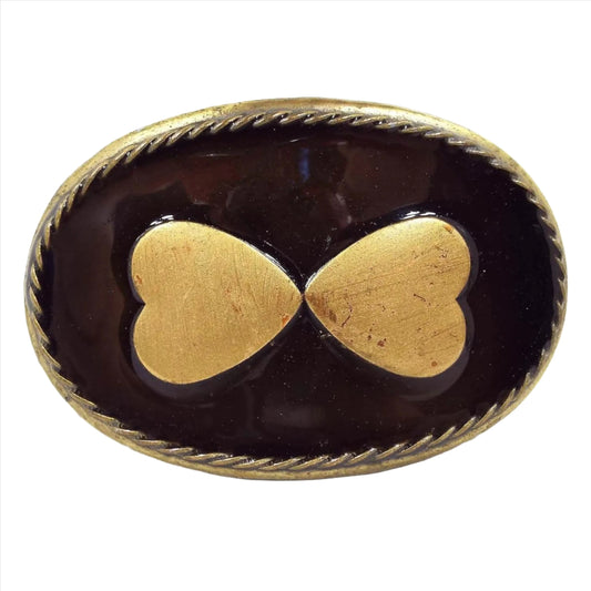 Front view of the Midwestern Mfg belt buckle. It is oval and antiqued brass in color. The front has two hears with the bottom of the hearts pointing inwards. The background on the front is enameled in dark brown.
