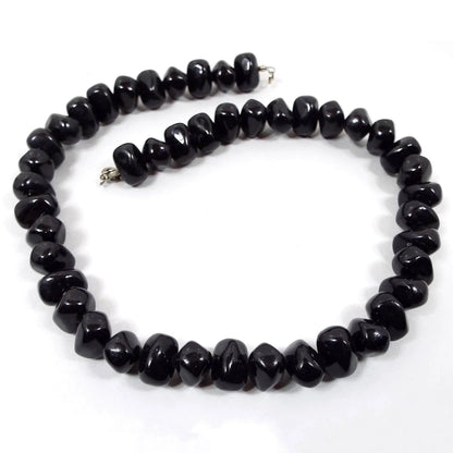 Front view of the retro vintage black beaded necklace. The beads are chunky nugget style black plastic beads. There is a silver tone spring ring clasp at the end.