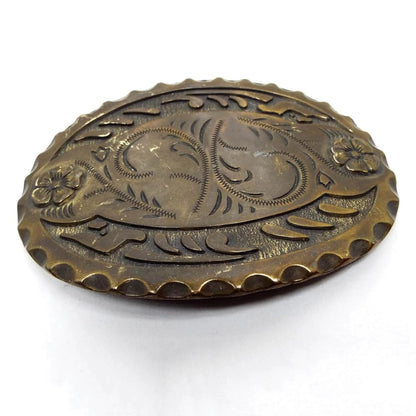 Front view of the retro vintage antiqued brass oval belt buckle. It has a scalloped edge and a cut floral design on the front.