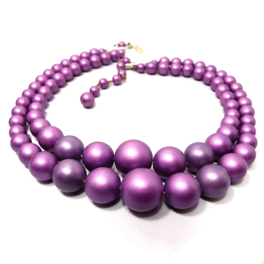 Angled view of the Mid Century vintage Japanese multi strand necklace. It is beaded with round matte shimmery beads in shades of bright purple. There is a hook clasp at the end.
