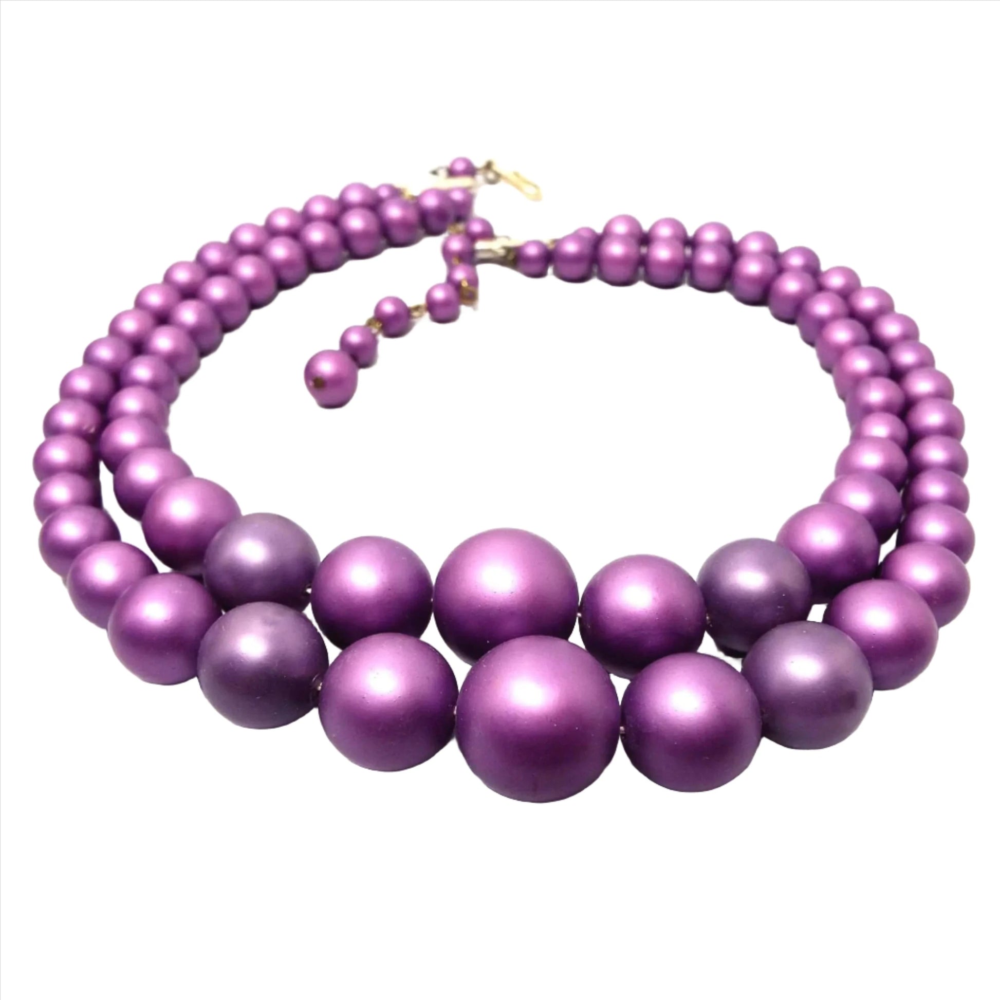 Angled view of the Mid Century vintage Japanese multi strand necklace. It is beaded with round matte shimmery beads in shades of bright purple. There is a hook clasp at the end.