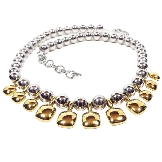Front view of the two tone retro vintage Monet metal beaded necklace. There are round silver tone color metal beads all the way down the necklace strung on a thin chain. The bottom part has gold tone color rounded square drops hanging down.