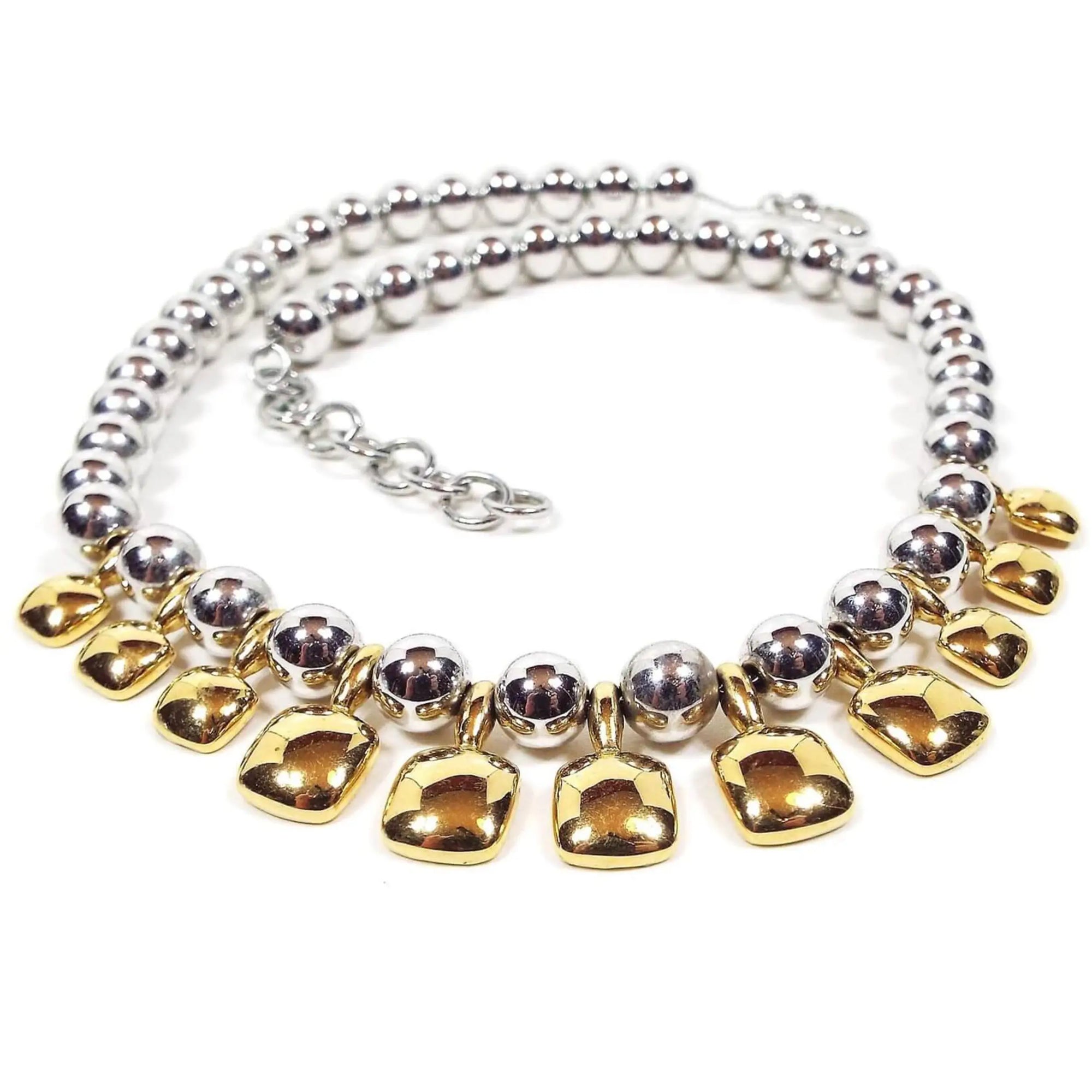 Front view of the two tone retro vintage Monet metal beaded necklace. There are round silver tone color metal beads all the way down the necklace strung on a thin chain. The bottom part has gold tone color rounded square drops hanging down.