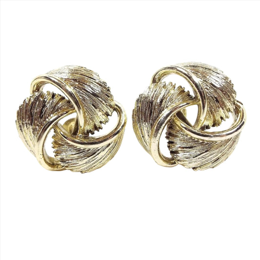 Front view of the Mid Century vintage Lisner screw back earrings. They are gold tone in color and look like three feather like areas that are twisted and curved around in a round type shape.